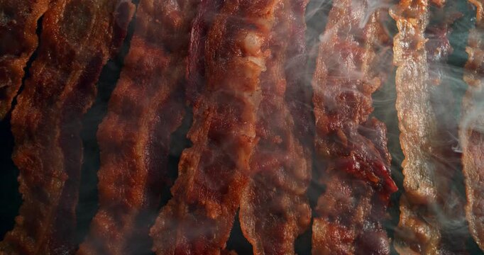Top-down cinematic view of crispy bacon sizzling and gently bouncing on a hot griddle, with aromatic smoke rising around it. A hypnotic, appetizing dance of texture, heat and flavor.
