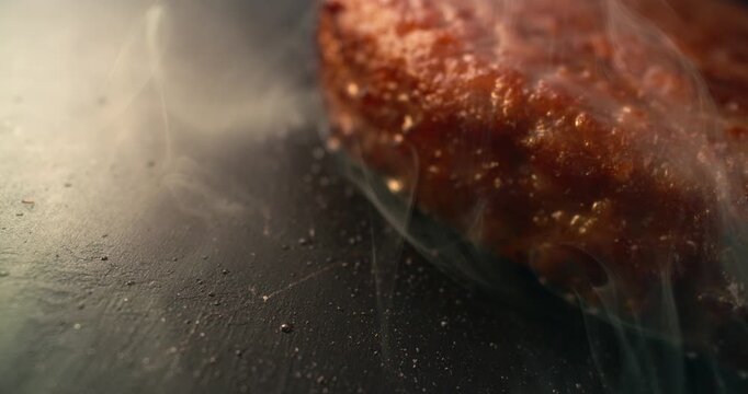 Cinematic macro of a juicy burger patty cooking on a blazing hot griddle, surrounded by rising smoke and sizzling heat. Rich textures, intense aroma and irresistible freshly cooked flavor.