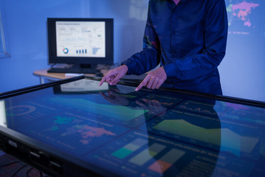 Businessman using a large interactive touchscreen table with charts and world map data in a modern blue-lit office.