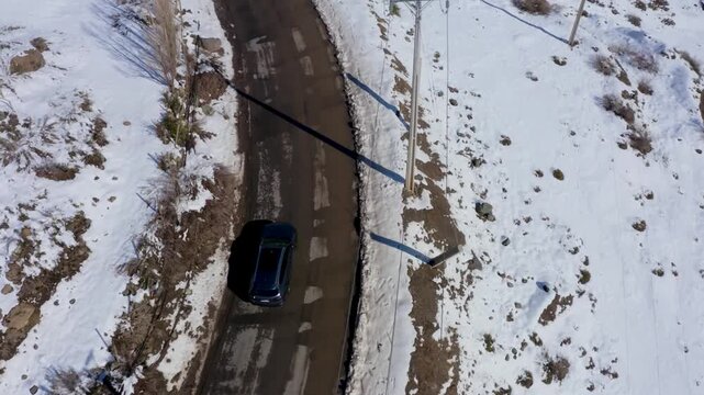 Drone footage of car driving on snowy mountain road with telephone poles.