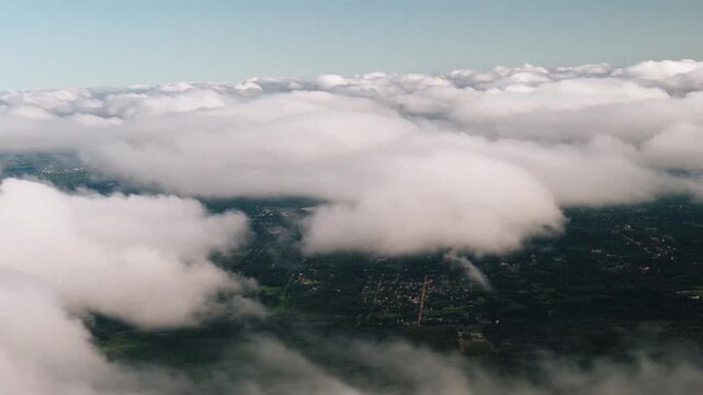 Aerial view of fluffy clouds floating over green landscape and small village.