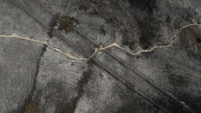 Aerial view of fire-damaged landscape showing scorched earth and a winding dirt path across the blackened terrain in Plevenon, Brittany, France.