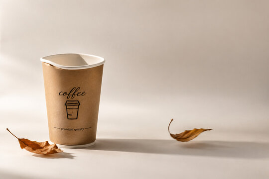 Disposable paper cup with deformed rim and dried autumn leaves in soft breeze, bright studio