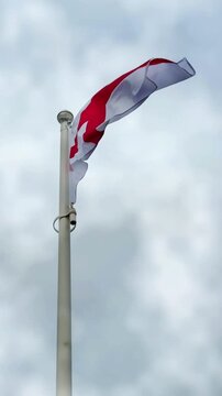 Vertical video social media - The national flag of England &ndash; Saint George&rsquo;s flag on a mast, blowing in the wind in slow motion, with red cross on white background, on an overcast day.