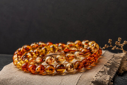 Honey-colored resin bead bracelet on linen cloth, organic plant inclusions, dark slate background, amber tones, jewelry presentation