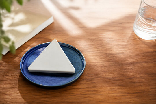 White equilateral triangle paperweight on blue ceramic coaster, neutral still life for editorial header