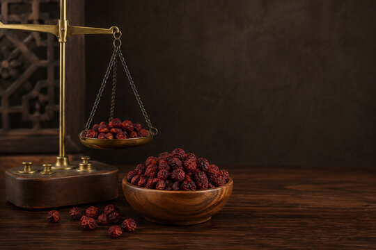Dried schisandra berries and brass balance scale on walnut counter, traditional apothecary concept