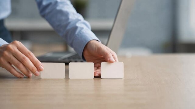Businessperson arranging blank white cards on wooden table with laptop in modern office setting