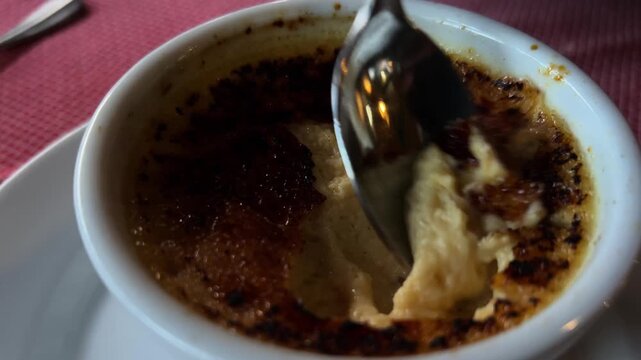 Close up of spoon digging into creamy creme brulee dessert with caramelized sugar top.