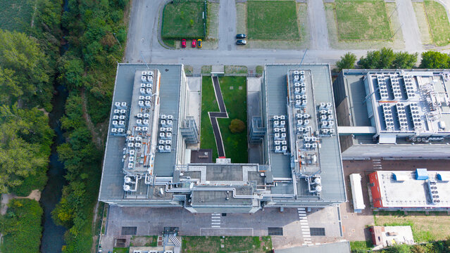 Aerial view of a modern data center facility featuring rows of rooftop HVAC units, a central green courtyard, and surrounding industrial infrastructure, Settimo Milanese, Lombardy, Italy.