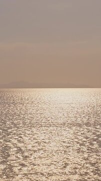 Vertical video. Golden Sunset Reflection Shimmering Across Calm Sea Surface With Gentle Waves and Distant Islands on Horizon