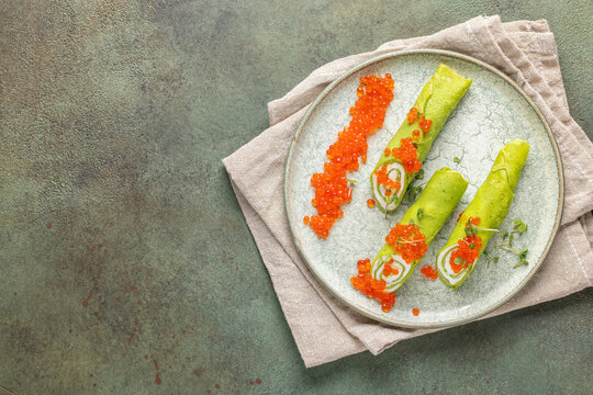 Spring green spinach crepes rolls with cream cheese and red caviar in plate on the table. Top view