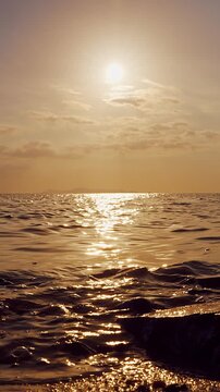Vertical video. Golden Sunset Above Rocky Shore With Gentle Sea Waves and Glowing Water Reflection, Low Angle Coastal Landscape, Peaceful Evening, Relaxation, Nature