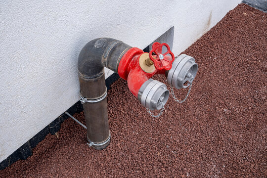 Red fire hydrant water pipe. Fire standpipe with dual hose couplings connection near building. Useful for fire safety, building infrastructure, emergency services, and construction publications.