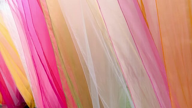Layers of translucent pink, orange, yellow, green and white fabric, creating an abstract composition of flowing textile, light and vibrant color, shot handheld. High quality 4k footage