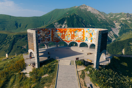 Aerial view of the Gudauri View Point monument, a circular stone structure with vibrant murals, set against lush green Caucasus Mountains in Ganisi, Mtskheta-Mtianeti, Georgia.