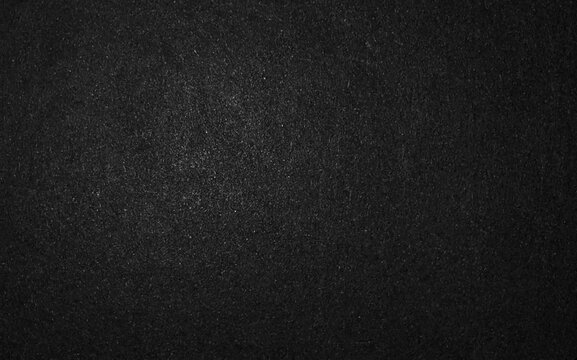 Dark black textured paper background or charcoal gray surface with fine grain.
