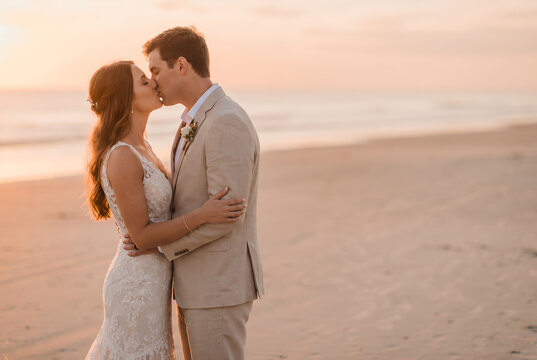 Bride and groom kissing on beach at golden sunset wedding ceremony