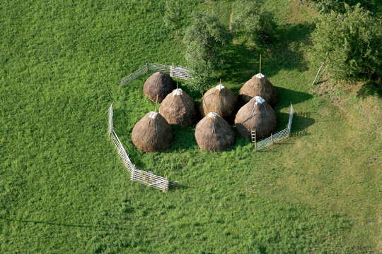 Aerial view of haystacks arranged in a green meadow surrounded by a wooden fence in Montenegro.