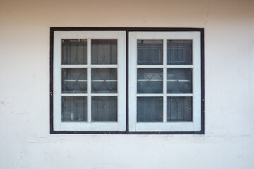 Fototapeta premium Close-up view of a classic white wooden window with multiple glass panes set into a plain concrete wall.