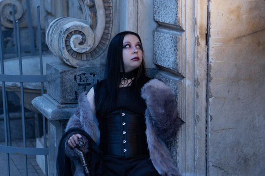 Gothic vampire woman in fur and corset resting at a stone wall, dark fantasy character image.