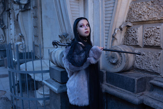 Woman in fur coat touching an old stone wall with cane in hand, exploring the old city.