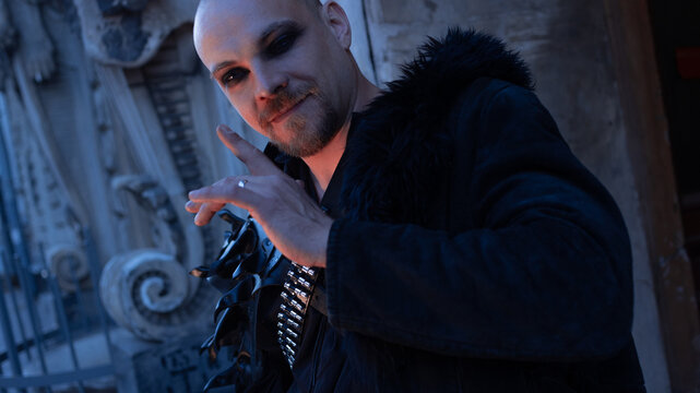 Tilted portrait of a man in dark makeup with raised hand, provocative and playful expression.