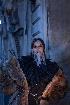 Stylish woman in chain face mask and leather feather cape, fur coat. Gothic fashion portrait