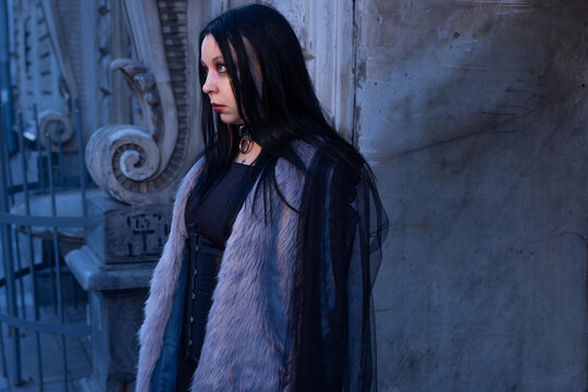 Profile portrait of a woman with black hair near an old wall, calm alternative style