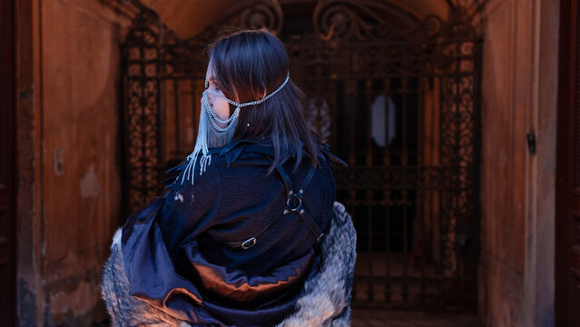 Back view of a woman in a leather harness and chain headpiece in an old doorway