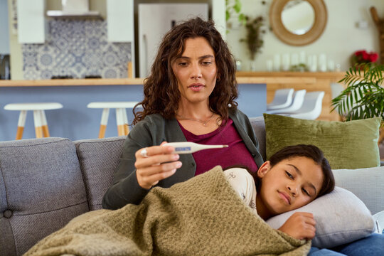 Worried mother checking daughter temperature at home