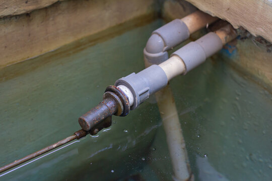 Close-up view of a metal brass float valve mechanism connected to PVC water pipes inside a tank