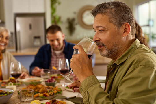 Mature man tasting red wine while sitting at dining table