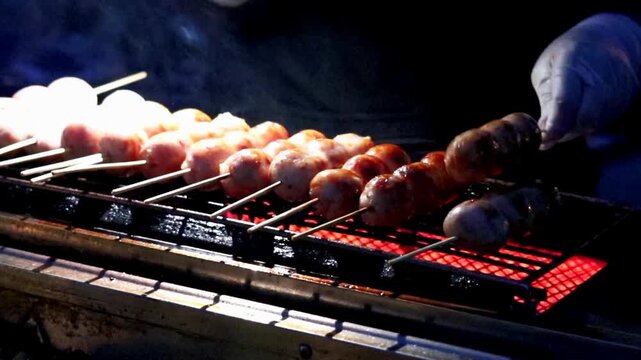 A street food vendor wearing white gloves grills skewered Sai Krok Isan, sour Northeastern Thai pork and rice sausage, checking each skewer over glowing charcoal at a night market stall.