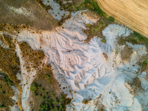 Aerial view of the pale eroded badlands and clay ravines meeting golden fields in the Spanish Pyrenees foothills Aragon Spain an abstract landscape of geology and time.