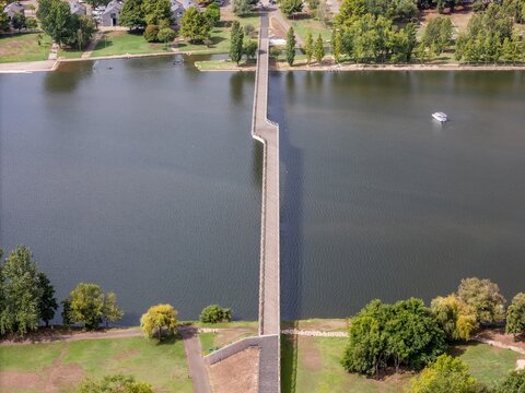 Aerial view of the modern Ponte Pedonal Pedro e Ines pedestrian bridge spanning the Mondego River, surrounded by lush green parks and trees in Coimbra, Coimbra, Portugal.