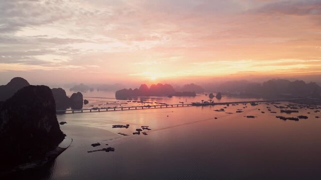 Aerial view of sunset over Ha Long Bay featuring Van Don bridge and karst limestone islands in Vietnam.