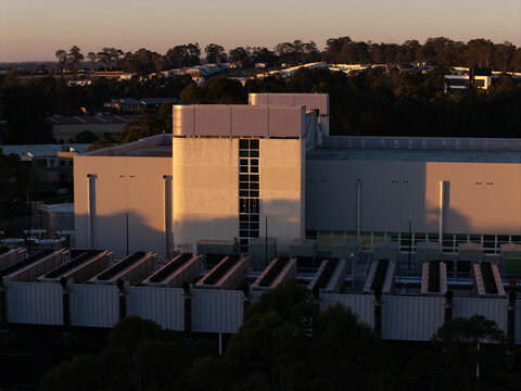 Aerial view of a modern data center facility during golden hour, featuring rooftop cooling units and surrounding greenery in Sydney, New South Wales, Australia.