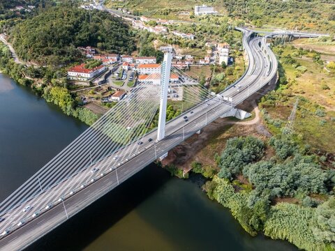 Aerial view of the Ponte Rainha Santa Isabel cable-stayed bridge spanning the Mondego River with highway traffic and surrounding green hills in Coimbra, Coimbra, Portugal.