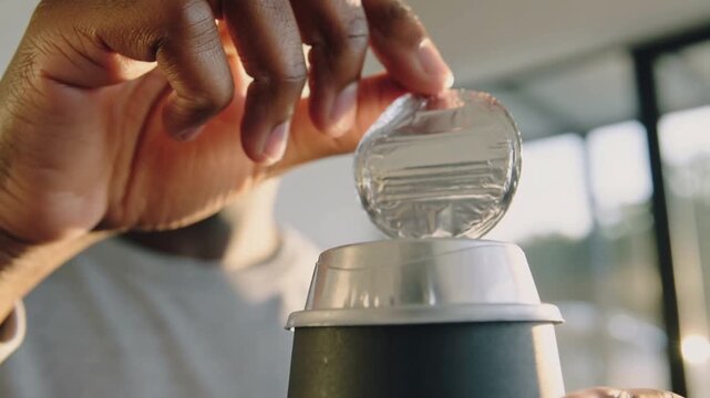 Peeling man hooking foil edge with finger, removing seal from cup by windows to access beverage