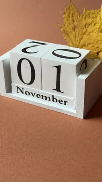 First of November date on white wooden calendar and tiny yellow maple baby leaves as symbols of beginning of the last fall month with terracotta background