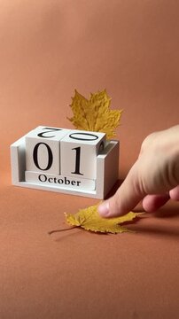 First of October date on white wooden calendar and tiny yellow maple baby leaves as symbols of beginning of the middle fall month with terracotta background