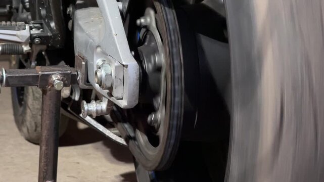 scene depicting rear motorcycle wheel spinning on stand with repair tools visible outdoors