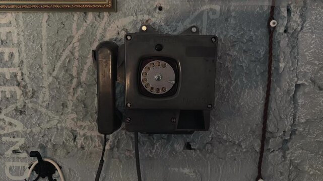 Old vintage Soviet industrial rotary telephone mounted on a grunge grey concrete wall inside an authentic retro communication room handheld orbiting arc shot capturing historical cold war details
