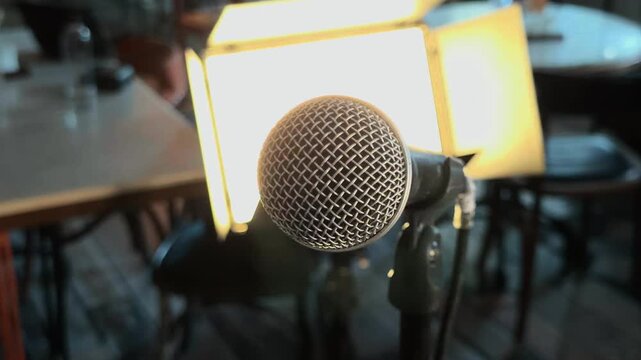 Professional dynamic microphone on stand with cinematic rack focus to bright LED video light panel inside empty cafe interior during documentary interview preparation handheld orbiting arc b-roll shot
