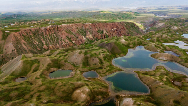 Aerial view of Tulpar Lake surrounded by rolling green hills, rugged cliffs, and small alpine pools in Alay District, Osh Region, Kyrgyzstan.