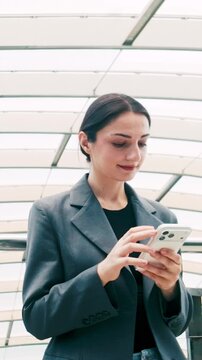 A professional in a gray blazer uses a smartphone beneath a modern glass roof, focused on the screen.