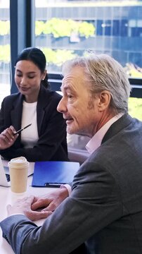 Experienced senior businessman speaks during a professional team meeting with a female colleague in a modern office, sharing ideas in a collaborative workplace.