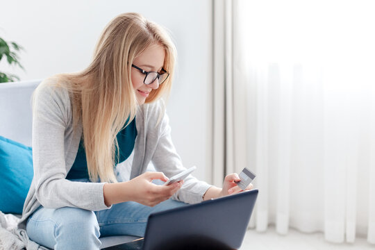 Woman paying by credit card with laptop, smartphone for purchases. Shopping online at home. Happy girl buy insurance, investing. Technology lifestyle. Finance, e-commerce, banking