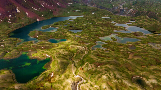 Aerial view of Tulpar Lake with its numerous small ponds nestled among rolling green hills and snow-capped mountains in Alay District, Osh Region, Kyrgyzstan.